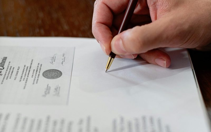 A detailed close-up photo of a hand signing a formal document with a pen, creating a professional agreement.
